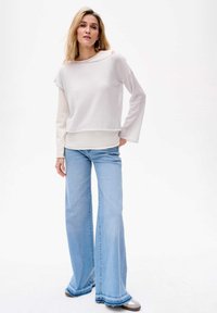 Hellgraues Langarmshirt mit weitem Ausschnitt und Cut-Out-Detail, kombiniert mit weit ausgestellten hellblauen Jeans mit fransigem Saum.