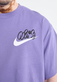 Fialové tričko s krátkým rukávem vyrobené z bavlny, s výrazným černobílým logem Nike na hrudi. Hladká textilie, uvolněný střih.