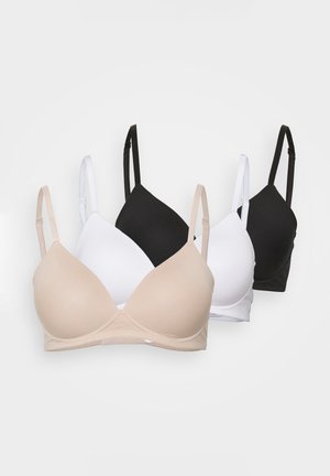 Kvinde iført beige bh og matchende undertøj, der viser overkrop og let løftet arm mod ensfarvet baggrund.