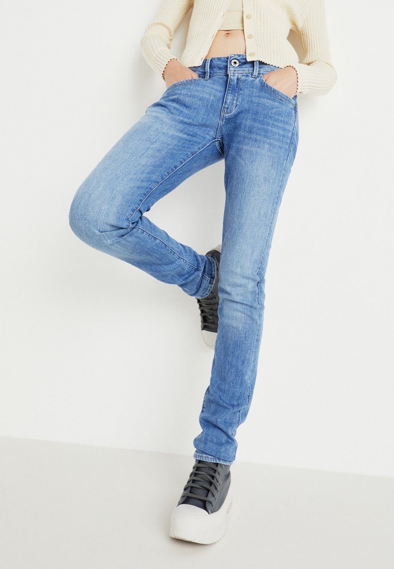 Jeans in denim azzurro chiaro con vestibilità slim, design a cinque tasche e leggera usura. Indossati con sneakers nere alte.