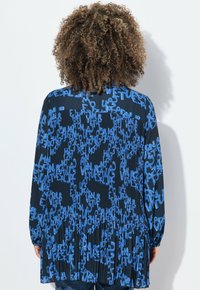 Blusa plissettata in tessuto blu navy con motivo testuale blu toroidale. Maniche lunghe con polsini elasticizzati e una vestibilità rilassata sul retro.