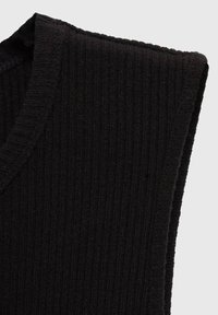 Haut sans manches noir à côtes, mettant en avant un col en V et un tissu tricoté texturé, soulignant une forme ajustée et des bords lisses.