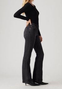 Jean noir taille haute en denim, avec une coupe slim au niveau de la cuisse, une jambe évasée, des coutures orange et des poches arrière.