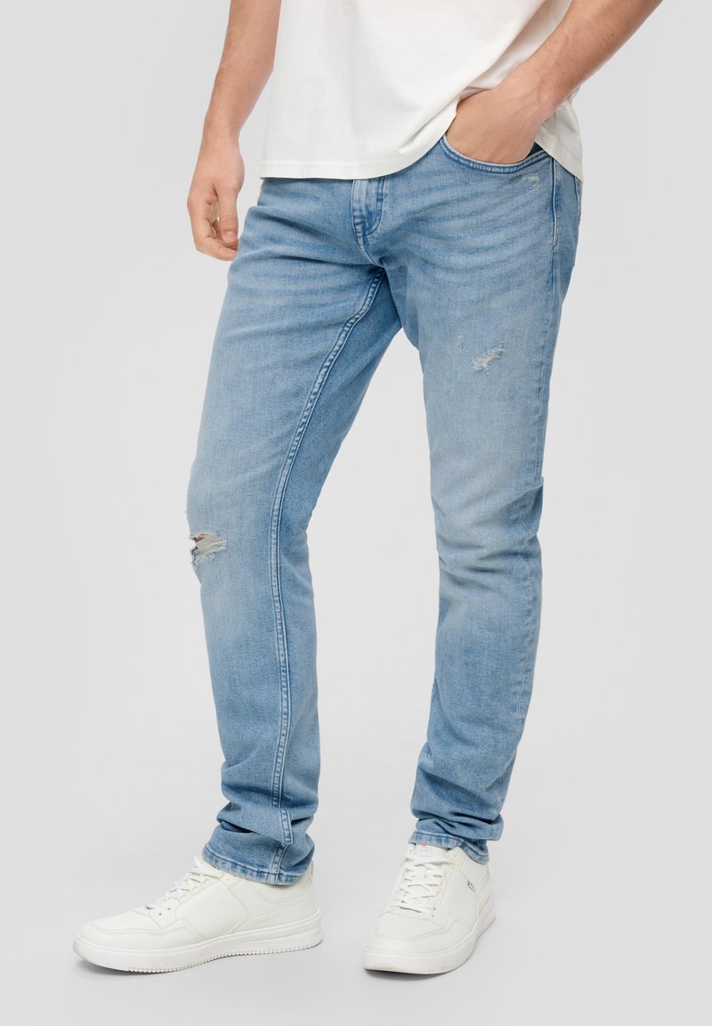 Jasnoniebieskie dżinsy o dopasowanym kroju, z przetarciami w okolicy kolan, w połączeniu z białymi sneakersami.