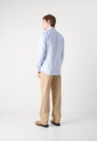 Light blue long-sleeve shirt paired with beige, loose-fitting trousers. Smooth fabric, relaxed fit, and minimal detailing on the shirt.