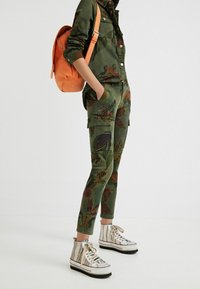 Gröna cargo-byxor med blommönster; kombinerade med randiga högtoppsskor. Den orange ryggsäcken ger en kontrasterande detalj.