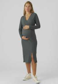 Zwangerschapswikkeljurk in donkergrijze ribstof met een zijsplit, gecombineerd met beige hoge sneakers. Lange mouwen en een V-hals ontwerp.