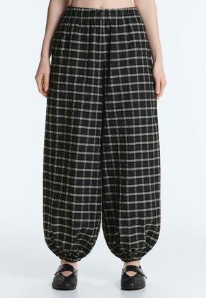 Čierno-biele kárované voľné nohavice s elastickým pásom a nazbieranými elastickými manžetami, nosené s čiernymi topánkami.