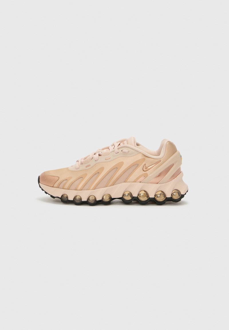 Baskets athlétiques beige avec des superpositions de design ondulées, des unités de semelle à coussin d'air visibles et un petit logo swoosh sur le côté.