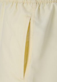 Helle gelbe Shorts aus weichem Stoff, mit einem elastischen Bund und einer Seitentasche mit sichtbaren Nähten. Glatte Textur.