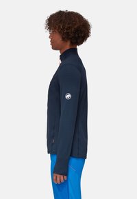 Navyblaue Zip-Jacke mit geripptem Textil, hohem Kragen und kontrastierendem orangefarbenem Reißverschluss; mit einem Logo auf dem linken Ärmel.