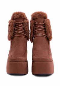 Stivali platform in suede marrone con un morbido colletto in pelliccia sintetica e lacci. Il design è angolare con una suola spessa per un'altezza aggiuntiva.
