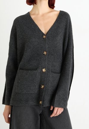 Cardigan en tricot gris avec un col en V, fermeture à gros bouton, deux poches avant et un motif ribbed texturé. Manches amples.