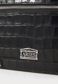 Borsa in pelle nera con stampa a coccodrillo, dotata di chiusura con zip argento e logo "ARIES" in rilievo argentato sul davanti.