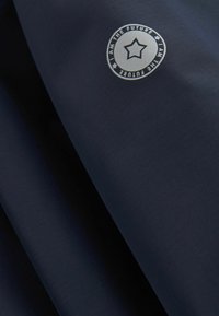 Pamučni materijal tamnoplave boje s teksturiranom površinom sadrži okrugli logo s natpisom "JA SAM BUDUĆNOST" i srebrnom zvjezdicom.
