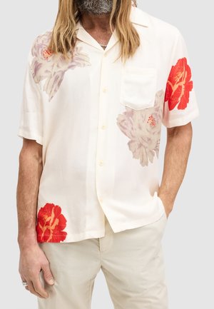 Camisa de manga corta de color crema con flores grandes en rojo y lila claro. Diseñada con un bolsillo, confeccionada en tela ligera.