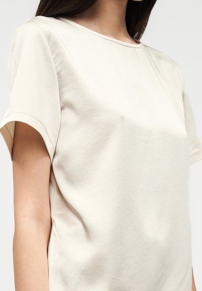 Ανοιχτό μπεζ κοντομάνικο πουκάμισο από μαλακό ύφασμα. Διαθέτει στρογγυλή λαιμόκοψη και ομαλή υφή, με ελάχιστες ραφές και άνετη εφαρμογή.