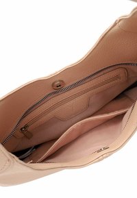 Gaišbeige ādas rokassoma iekšpuse ar rāvējslēdzēja kabatu un divām atvērtām nodalījumiem. Mīksta tekstūra, šūtas malas un pogu aizdare.