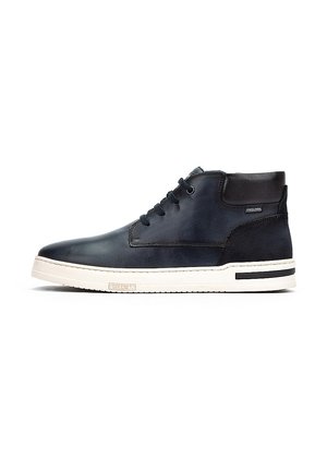 Zapatos de cuero negro hasta el tobillo con un acabado suave, suela de goma blanca en contraste y detalles negros en el talón y los laterales. Cordones gruesos y redondos.