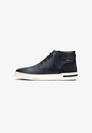 Chaussures noires en cuir à cheville avec une finition lisse, semelle en caoutchouc blanche contrastante, et accents noirs sur le talon et les côtés. Lacets épais et ronds.