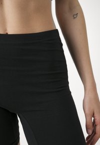 Fekete, magas derekú leggings rugalmas anyagból, sima felülettel, testhez simuló kialakítással, varrat nélküli derékkal és oldalvágott részletekkel.