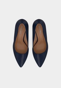 Μπλε ναυτικού παπούτσια με μυτερή μύτη από δερμάτινο γυαλιστερό, με λεία επιφάνεια και ανοιχτές πλευρές. Διαθέτουν καφέ εσωτερική σόλα με ανάγλυφο λογότυπο.