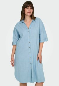 Robe chemise en lin bleu clair avec un front à boutons, un col pointu et des manches retroussées avec des accents de boutons. Coupe décontractée.