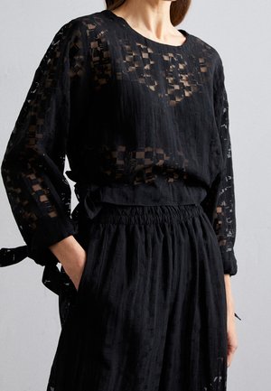 Zwarte blouse van doorzichtig, textuurmateriaal met een geometrisch patroon. Relaxte pasvorm, ronde halslijn en lange mouwen. Elasticiteit in de taille.