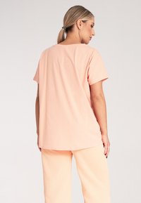 Brzoskwiniowy, krótki rękaw koszulka z luźnym krojem, wykonana z miękkiego materiału, z okrągłym dekoltem i gładką teksturą.