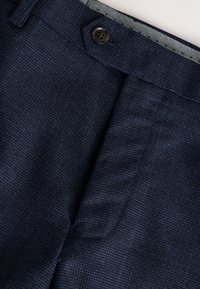 Temno modre hlače z teksturirano tkanino, z eno gumbno zapiranjem in subtilnim vzorcem ribje kosti na pasu.