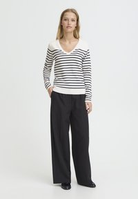 Pull à col en V à rayures crème et marine, associé à un pantalon noir taille haute à jambes larges, présentant une coupe décontractée et un design minimaliste.