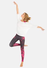 White loose-fit top with pink accents paired with black leggings featuring a pink geometric pattern. Model in a dynamic pose.
