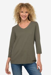 Oliwkowa, długosleeve'owa bluzka z dekoltem w serek, wykonana z miękkiego materiału. Posiada luźny krój z lekkim zaokrągleniem u dołu oraz subtelnym detalem logo na dole.