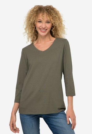 Maglietta a maniche lunghe verde oliva con scollo a V realizzata in tessuto morbido. Presenta una vestibilità rilassata con una leggera curvatura all'orlo e un discreto dettaglio del logo nella parte inferiore.