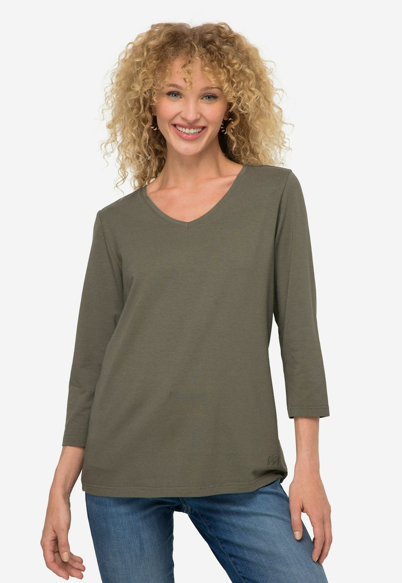 Oliwkowa, długosleeve'owa bluzka z dekoltem w serek, wykonana z miękkiego materiału. Posiada luźny krój z lekkim zaokrągleniem u dołu oraz subtelnym detalem logo na dole.