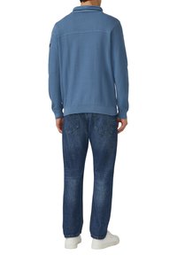 Niebieski sweter z dzianiny z prążkowanym kołnierzem, zestawiony z ciemnoniebieskimi dżinsami. Sweter ma teksturowane plecy i jest noszony z białymi trampkami.