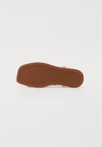 Brun gummi såle med en teksturert overflate, med en buet design og logo-inntrykk. Lys tan overmateriale synlig på sidene.
