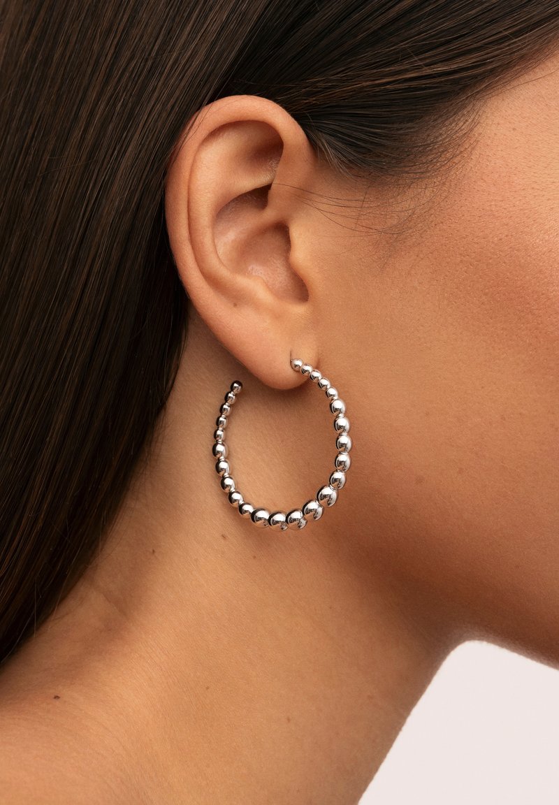 Pendientes de aro de plata con un diseño de cuentas, forma circular y superficie pulida, sujetos a una oreja.