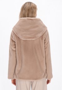 Giacca in finta pelliccia beige con grande cappuccio, maniche lunghe e vestibilità rilassata. Tessuto morbido e superficie liscia senza accessori visibili.