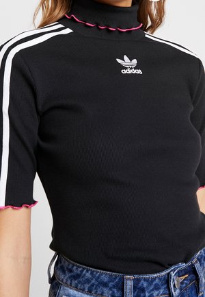 Top de cuello alto negro acanalado de Adidas con rayas blancas en las mangas, bordes fruncidos rosas, combinado con vaqueros de denim azul.