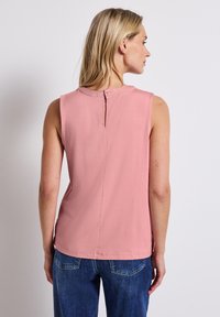 Top sans manches rose avec un col rond, une fermeture par bouton au dos et un ourlet droit. Le tissu semble lisse et léger.