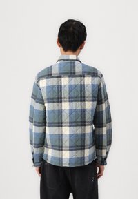 Quilted plaid jacket in blue, gray, and white tones. Features a classic collar and button cuffs with a rectangle diamond pattern on fabric.