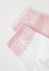 Κάλτσες από βαμβακερό μείγμα με ριμπέ με ροζ μπορντούρα και λευκή επιγραφή, που αντιδιαστέλλεται με λείο λευκό σώμα.