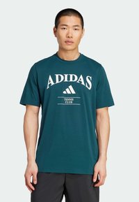 Turkusowa bawełniana koszulka z krótkim rękawem i okrągłym dekoltem, z białym logo "ADIDAS" oraz tekstem "TENNIS CLUB" w wyraźnym wzorze.