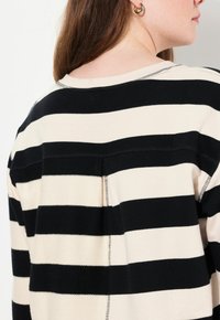 Maglione a righe in nero e beige, con spesse righe orizzontali, tessuto morbido e dettagli a punto lungo il collo e le maniche.