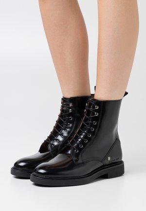 Black leather ankle boots with a glossy finish, featuring a lace-up front, silver hardware, and a sturdy black rubber sole.
