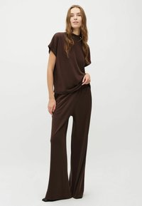 Bruine, losse T-shirt met korte mouwen en een hoge halslijn, gecombineerd met bijpassende broek met wijde pijpen, beide in een zachte, gladde stof.