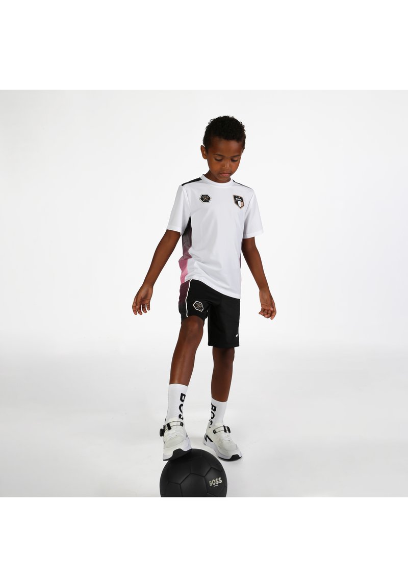 Jersey blanca de manga corta con acentos negros y rosas, combinada con pantalones cortos negros y calcetines blancos con texto. Balón de fútbol negro a los pies.