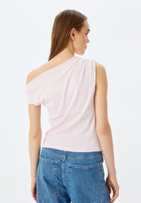 Asymmetrisk rosa topp med korta ärmar, mjuk textur och bred halsringning, kombinerad med blå denimshorts med bakfickor.