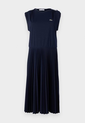 Vestido azul marino fabricado en una tela suave, con falda plisada, mangas cortas y un pequeño logo en el pecho. Textura lisa en todo el vestido.